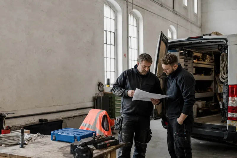Zwei Handwerker prüfen einen Auftrag neben ihrem Servicefahrzeug.